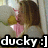 Pixelated image of a person with brown hair wearing pink clothing and holding a yellow object, with text 'ducky:]' at the bottom.