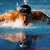 A swimmer in mid-stroke with arms extended forward, head submerged under blue water surface.