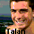 Pixelated static image of a person with light skin tone wearing dark sunglasses, smiling broadly against a blurred background featuring green and blue tones.