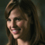 Pixelated close-up of a person with long brown hair smiling, showing teeth, against a dark background.