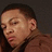Pixelated close-up of a person with short dark hair, light skin, and a neutral expression against a dark background.