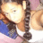Pixelated static image of a character with light skin, dark hair tied in a ponytail, wearing blue clothing and holding an object near the face.