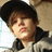 Pixelated close-up of a person with brown hair wearing dark clothing against a light background.