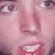 Pixelated close-up of a person's face showing eyes, nose, and mouth with visible teeth, rendered in pink and red tones.