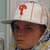 A pixelated close-up of a person wearing a white cap with red 'P' logo, dark sunglasses, and patterned clothing against blurred background.