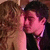 Two figures in close physical proximity, one with light brown hair and the other with dark hair, sharing a kiss.