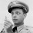 Black-and-white pixelated image of a person wearing a cap and bow tie, holding an object near their face.