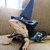 A pixelated figure wearing a tall blue witch hat, dark clothing, and holding a broomstick against a blurred background.