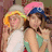 Two people in casual clothing pose together with one wearing a pink and blue hat, against a light orange background with pink text.