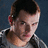Pixelated image of a person with short brown hair wearing a gray shirt, alongside red symbols and text on black and gray backgrounds.
