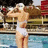 Pixelated image of a person in a white swimsuit standing on a dock by water, with a blurred background of structures and colors.