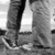 Black-and-white pixelated image showing two pairs of legs in dark pants and white shoes standing on a textured surface.