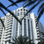 Pixelated image of a tall building with columns under a blue sky, framed by dark tree branches.
