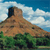 Pixelated landscape with brown rocky hill, green vegetation, blue sky, and white clouds.