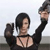 Pixelated image of a person with short dark hair wearing a black long-sleeve top with a cutout design, arms raised in a dynamic pose against a light background.