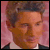 Static pixelated icon of a person with light brown hair and fair skin against a pink background, wearing dark clothing with visible collar.