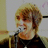Pixelated static image of a person with light brown hair wearing a dark top, positioned against a light background with a vertical yellow element on the left.