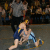 Pixelated image of a person in blue wrestling attire performing a move on another figure against a dark background.