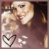A pixelated image of a smiling woman with long dark hair holding a small light-colored dog, with a black heart outline in the lower left corner.
