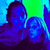 Pixelated static image of two figures in blue and purple tones against a green-to-blue gradient background.