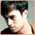 Pixelated close-up of a person with dark hair, light skin, and a black top against a muted blue-gray background.