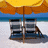 Beach scene with yellow umbrellas and striped lounge chairs, text changes from 'lets get' to 'away' with small wave symbols.