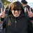Pixelated image of a person with brown hair wearing dark clothing, making two hand gestures against a blurred background.