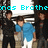 Six figures in dark and light clothing stand in a with two wearing blue shirts, under cyan text reading 'nas Brothe' and 'S.O.S' on a white background
