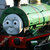Pixelated image of a blue-gray train engine with black eyes and a red front, set against a blurred green and white background.