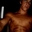 A pixelated image of a shirtless male figure with brown skin holding a white cylindrical object against a black background.