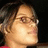 Pixelated close-up of a person with light skin tone, brown hair, and glasses, wearing a red garment against a dark background.