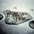 Pixelated grayscale image of a stylized vehicle with visible text elements on its side, set against a light background with scattered circular shapes.