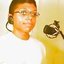 Pixelated static image of a person wearing glasses and large hoop earrings with a microphone icon on the right side, set against a gradient background.