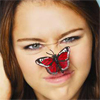 A close-up of a person with brown hair and blue eyes, featuring a red and black butterfly on their nose.