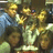 Pixelated static image of multiple figures in warm tones with blue and green accents, appearing to be a group scene.