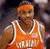 Pixelated image of a person wearing an orange basketball jersey with white trim, standing against a dark background.