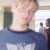 Pixelated static image of a person wearing a dark blue shirt with light-colored text, set against an indistinct background.