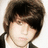 A pixelated image of a person with brown hair and dark bangs, wearing a black jacket over a white shirt against a light background.