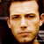 Static pixelated close-up of a person's face with brown hair and neutral expression on dark background.