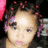 Pixelated close-up of a person with light skin tone, dark curly hair, and pink accents in hair, against a dark background with scattered pink and purple pixels.