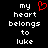 Black background with white pixelated text reading 'my heart belongs to luke' and a red pixelated heart symbol above 'my' on the left side.