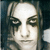Static pixelated image of a person's face with dark eye makeup and light hair against a dark background.