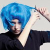 A person with bright blue hair holds a section of hair with scissors against a light gray background.