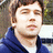 Pixelated close-up of a person with brown hair wearing a dark blue jacket over white clothing, set against an indistinct background.