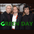Three pixelated figures in dark suits with white shirts and red accents stand side-by-side under a gray structure, green text reading 'GREEN DAY' below.