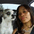 A pixelated image shows a person with long dark hair and light skin standing next to a white dog with black markings on its face, both facing forward against an outdoor background.