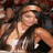 A woman with long dark hair appears in two distinct poses: one seated among a crowd, another standing against a light background.