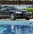 Static pixelated image of a dark sedan on a road with a blurred background of greenery and sky.