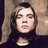 Pixelated image of a person with long hair against a textured background, accompanied by pink text and emoticon on black.