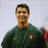 Pixelated image of a person in dark green clothing with a light circular emblem on the chest, against a pale background.